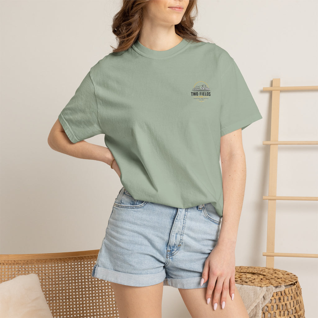 Model wearing sage green short-sleeve T-shirt with small Two Fields Co. logo